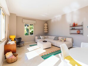 Een moderne woonkamer met een hoekbank, een eettafel en een inbouwkast met decoratieve objecten.