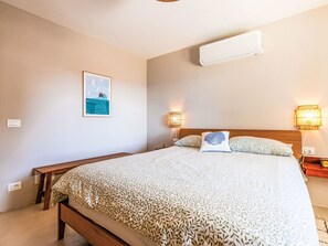 Ein Hotelzimmer mit einem Bett, Nachttischlampen, einer Wand-Klimaanlage und einem gerahmten Bild.