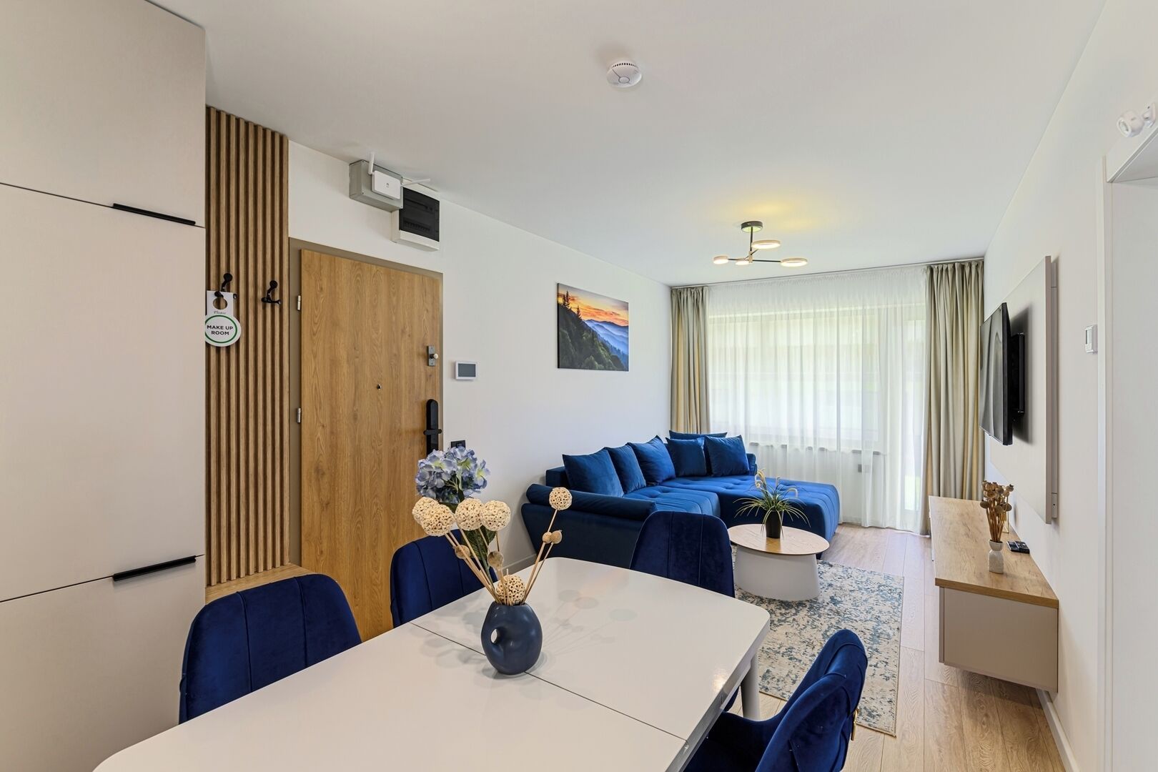 A modern living room with a sofa, a dining table, and a TV mounted on the wall.