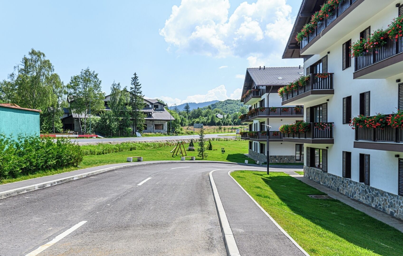 Un edificio a più piani con balconi, una strada curva e vegetazione.