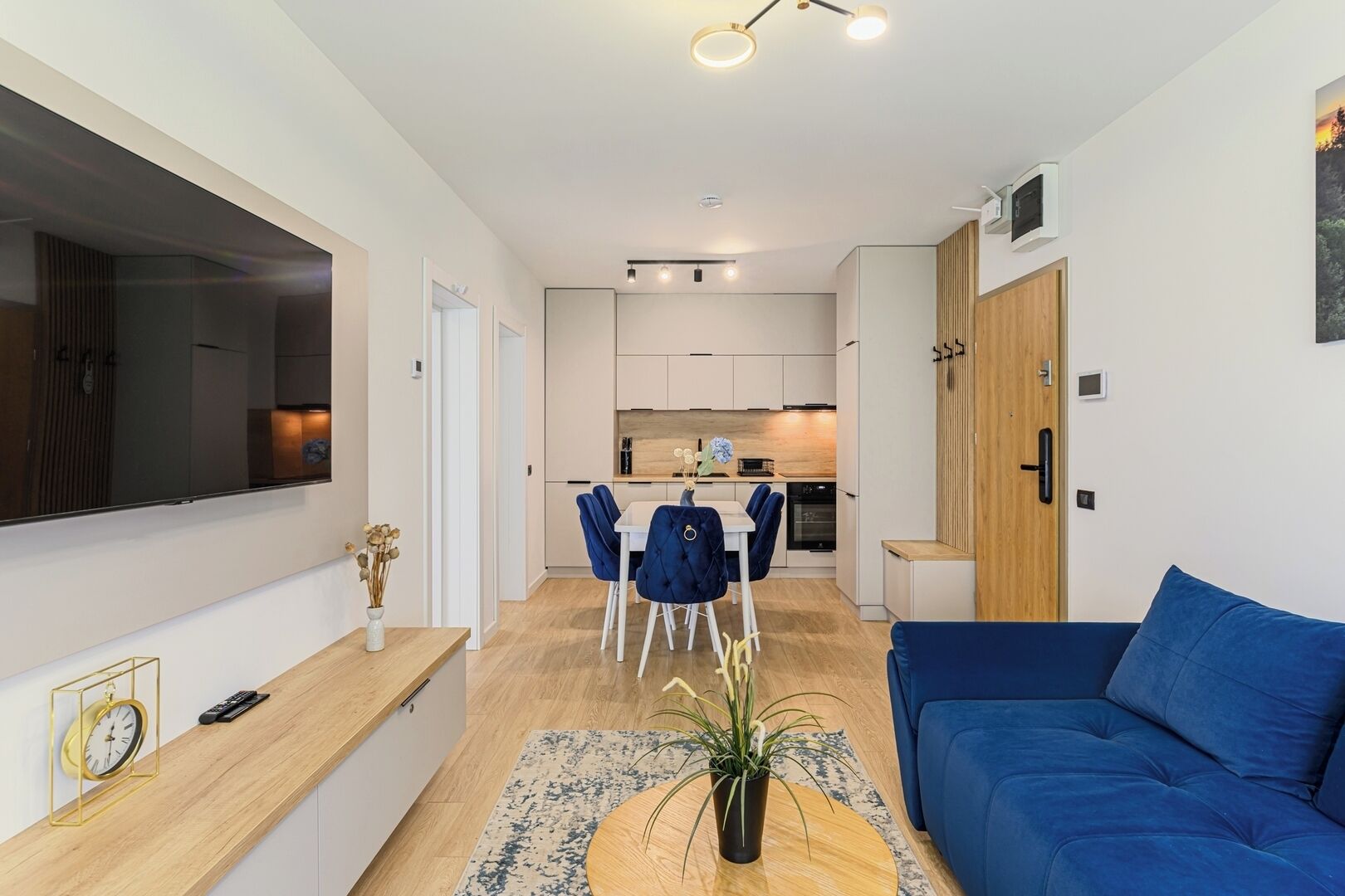 A modern living room with a blue sofa, a dining area with chairs, and a kitchen in the background.