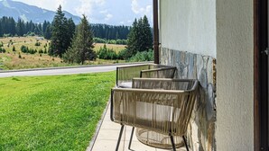 Een balkon met rieten stoelen met uitzicht op een weg en een bergachtig landschap.