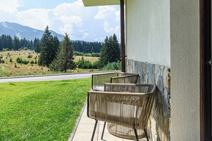 A balcony with wicker chairs overlooking a road and a mountainous landscape. - Art by Grand Chalet (Brașov)