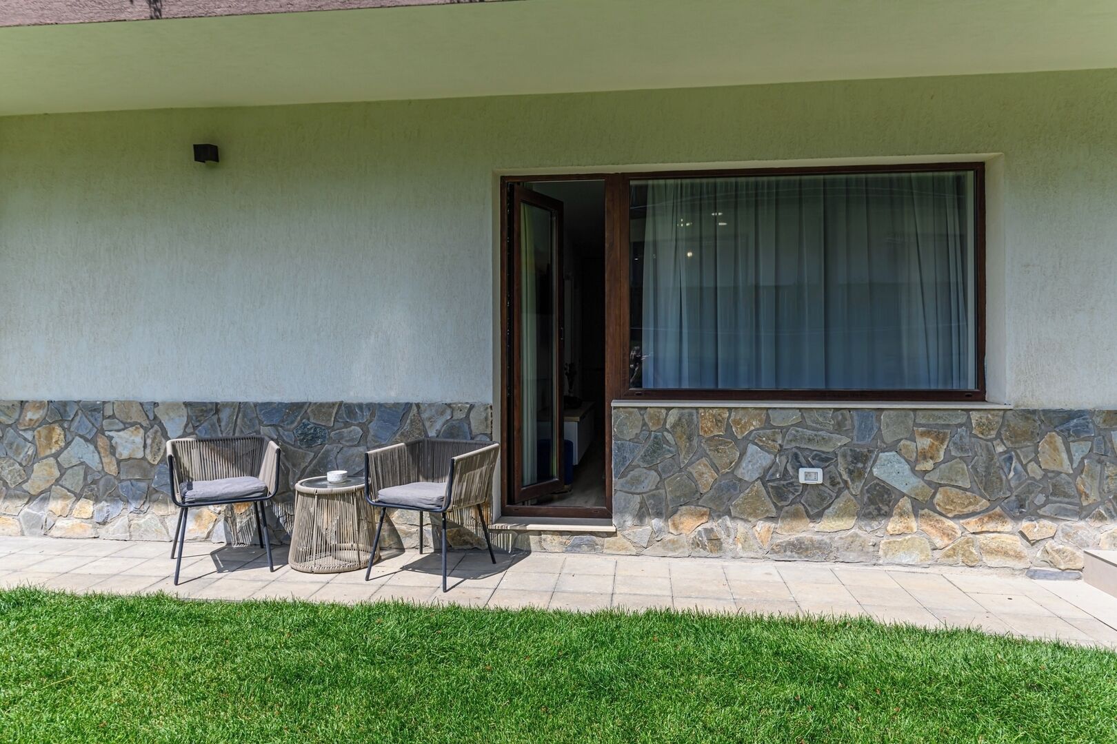 A patio with a stone wall, a glass door leading inside, and a small table with chairs.