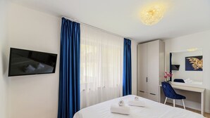 Hotelkamer met een bed, bureau, stoel, televisie en groot raam met gordijnen.