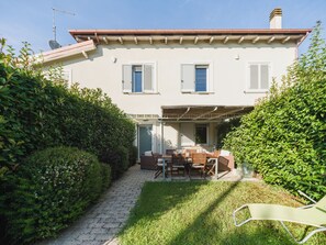Ein zweistöckiges Haus mit einer Terrassenfläche, einer Tür zu einem überdachten Außenbereich und einem kleinen Garten.