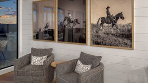 A room with a large window, two armchairs with patterned cushions, and three framed black and white horse riding photographs on the wall.