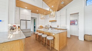 A modern kitchen with a central island, bar stools, wooden ceiling, and white cabinetry.
