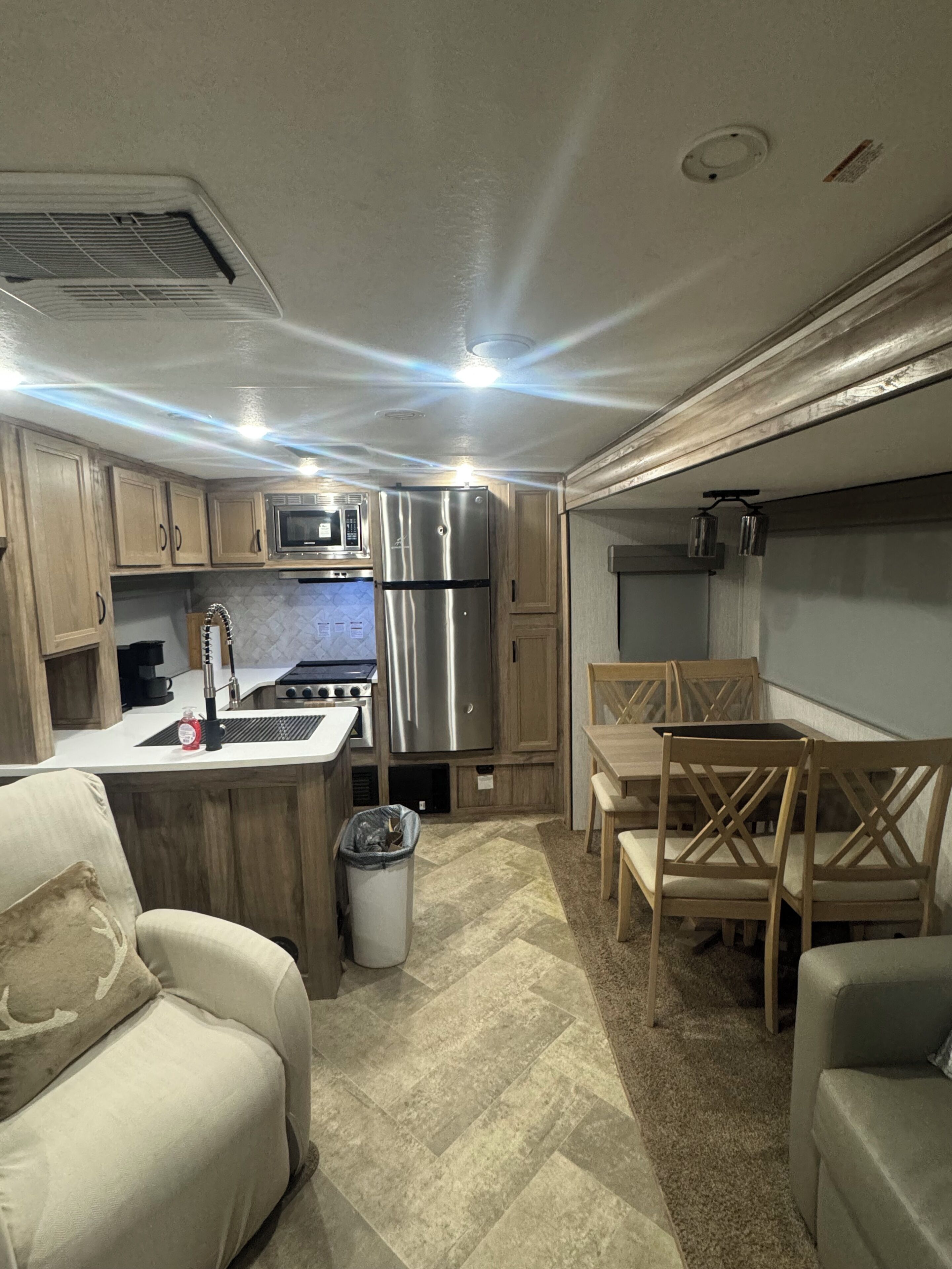A compact RV kitchen with a refrigerator, microwave, sink, and stove. There is a dining area with a table and chairs.