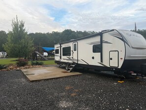 Un camping-car solaire équipé d’une rampe d’accès, d’un patio couvert et offrant une vue sur les arbres et un ciel bleu.