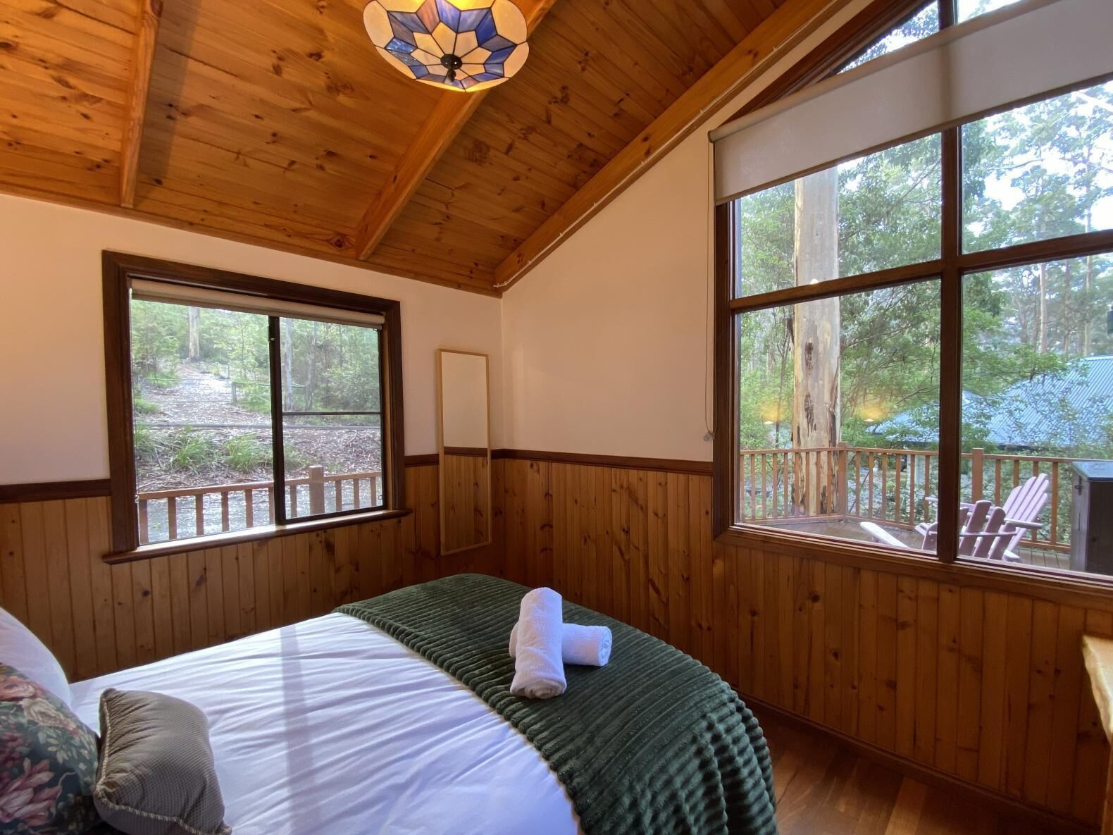 A wooden-paneled room with a bed, large windows, and a view of the outdoors.