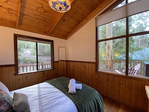 A wooden-paneled room with a bed, large windows, and a view of the outdoors.