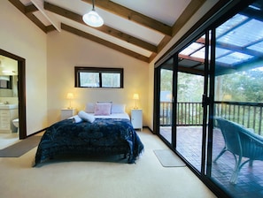 A bedroom with a bed, two bedside lamps, a window, and a balcony with chairs.