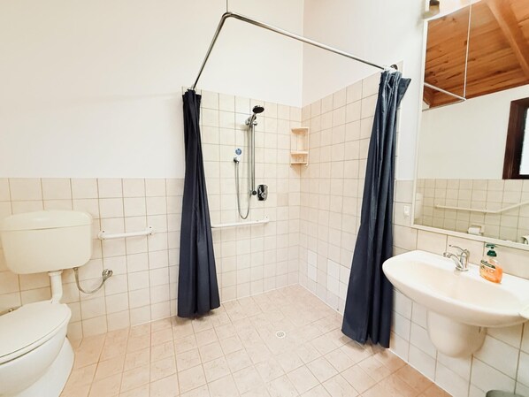 A bathroom with a toilet, sink, shower, and a wooden ceiling.