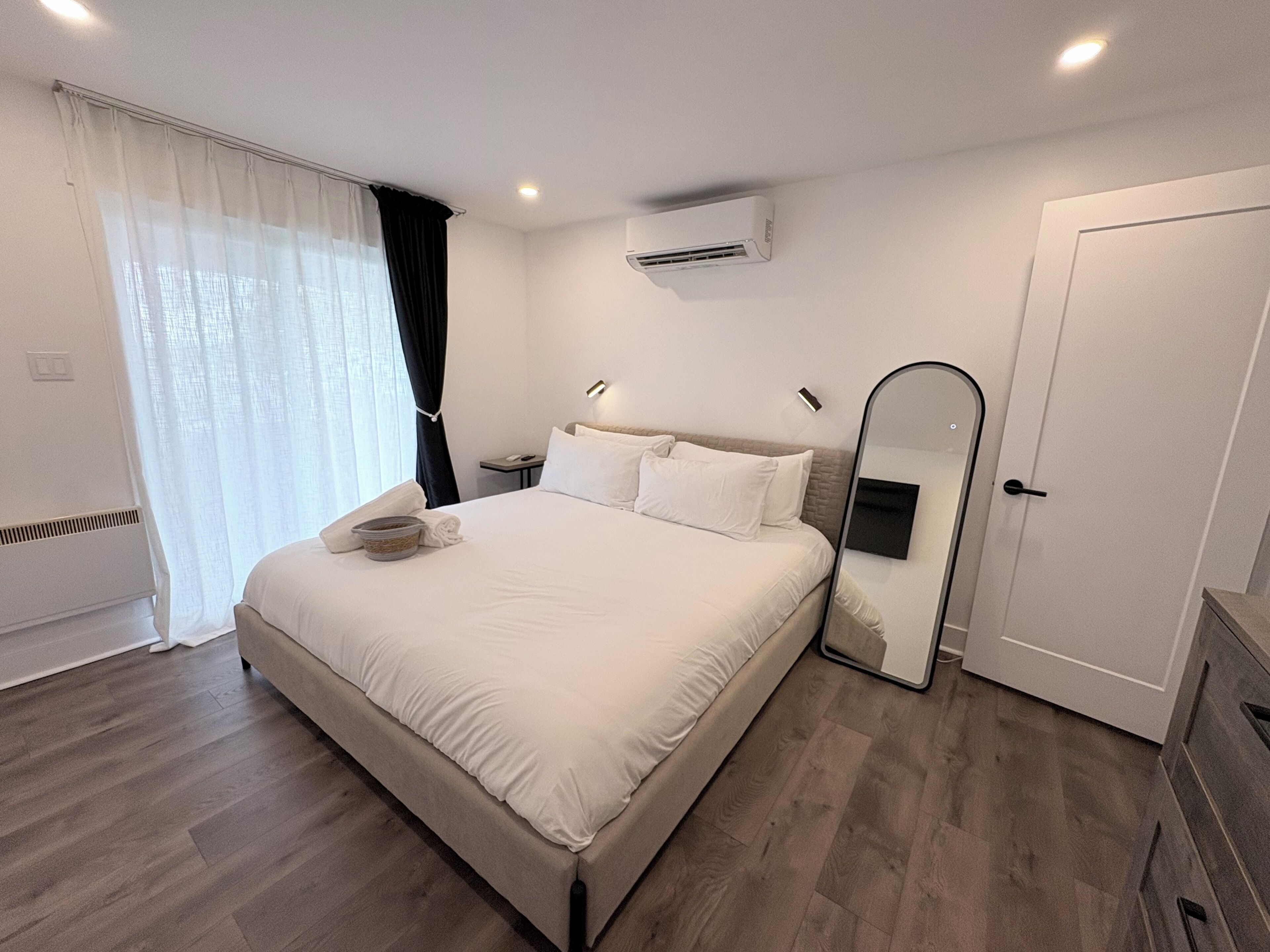 Une chambre d’hôtel moderne équipée d’un grand lit, d’une table de chevet, d’un miroir et d’un appareil de climatisation.