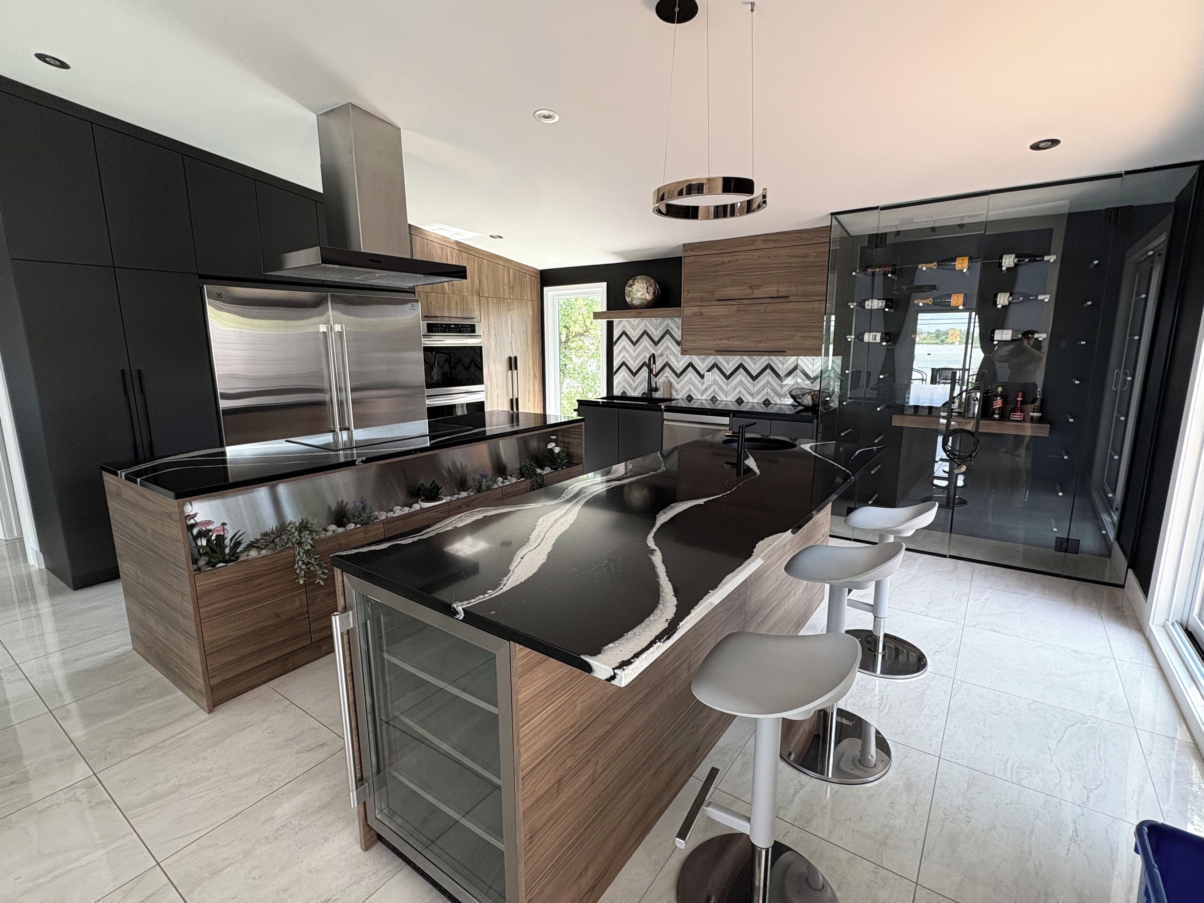 A modern kitchen with a central island, bar stools, and a glass-enclosed dining area.