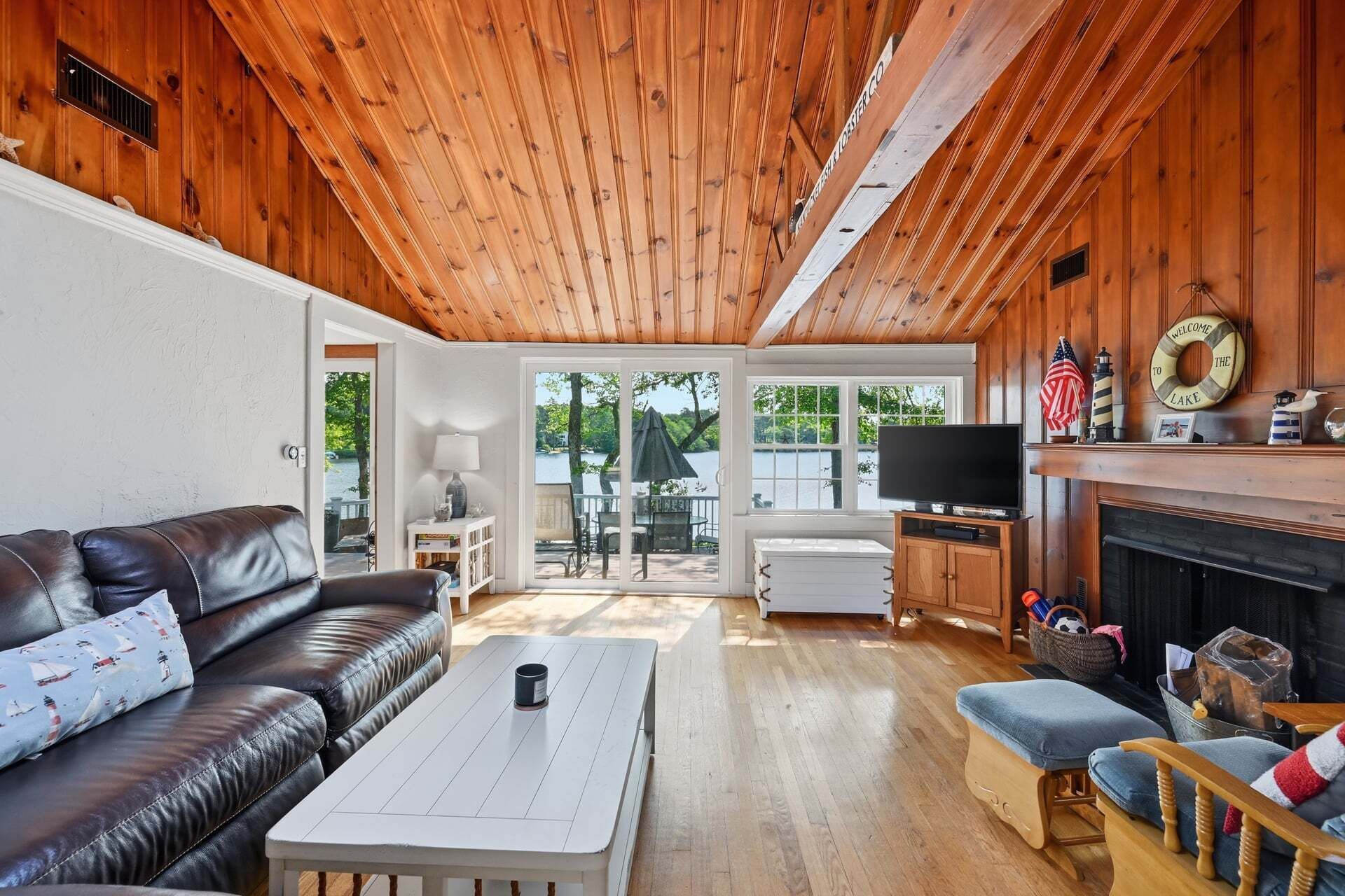 A cabin interior with a wooden ceiling, a leather sofa, a TV, a fireplace, and a view of the outdoors.