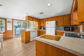 A kitchen with wooden cabinets, a white refrigerator, a stove, a microwave, and a sink. - Whispering Waters on Bearse Pond (Centerville)
