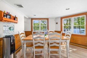 A dining area with a wooden table and white chairs, a water dispenser, and a bottle rack. - Whispering Waters on Bearse Pond (Centerville)
