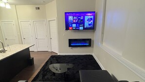 Uma sala de estar moderna com televisão de tela plana na parede, um sofá de couro preto, uma mesa de centro de vidro e um tapete preto.