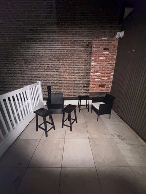 Ein Patio im Freien mit einer Backsteinmauer, einer weißen Brüstung und schwarzen Möbeln, darunter ein Tisch und Stühle.