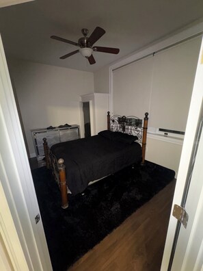 Une chambre à coucher comprenant un lit, un ventilateur de plafond, un radiateur et une porte donnant sur une autre pièce.