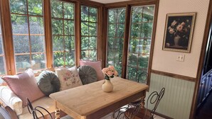 A dining area with a wooden table and chairs, a sofa with cushions, and a window with a view of trees. - Charming 4-bedroom lake cabin with a dock + AC in Excelsior (Excelsior)