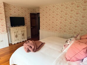 Un dormitori amb un llit, una televisió damunt d'una cómoda i paper pintat amb motius florals.