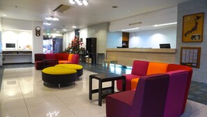 Een hotel lobby met een receptiebalie, kleurrijke zithoeken, een klok en een groot raam.