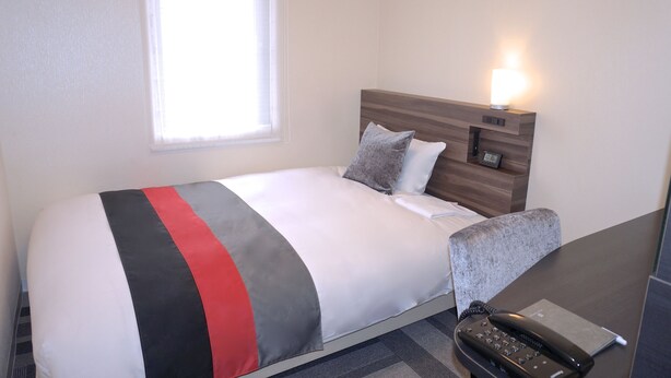 Een hotelkamer met een bed, nachtkastje, lamp en telefoon.