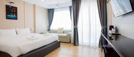 Una habitación de hotel moderna con una cama grande, un sofá, un televisor de pantalla plana y un amplio ventanal con cortinas.