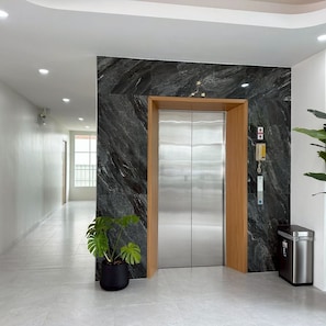 A modern elevator with a marble wall, a potted plant, and a trash bin. - Dview Golden Triangle Hotel Chiangsaen (Chiang Saen)
