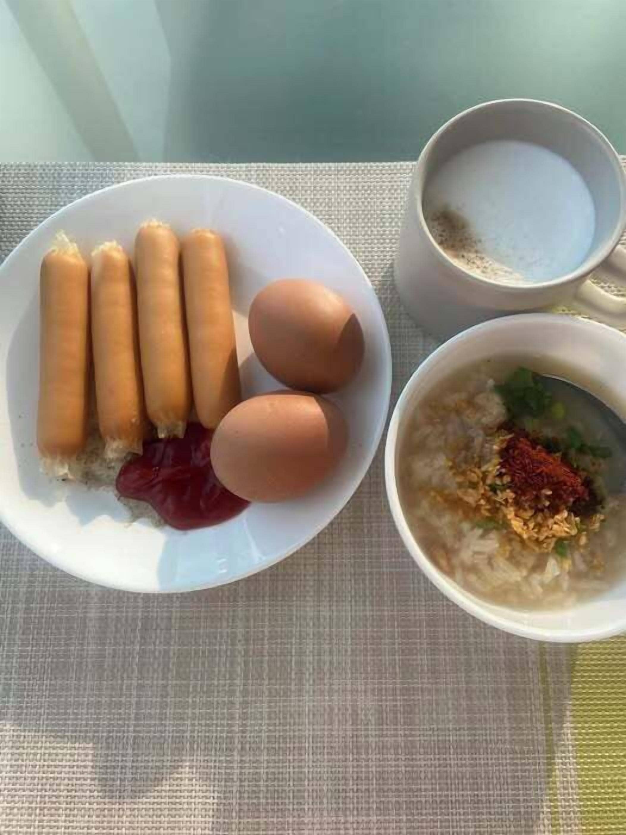 Un plato con salchichas y huevos, un tazón de sopa de verduras y una taza de té sobre una mesa.