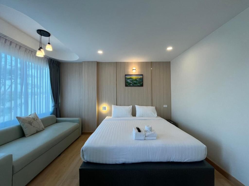 A modern hotel room with a large bed, a sofa, a painting on the wall, and a window with curtains.