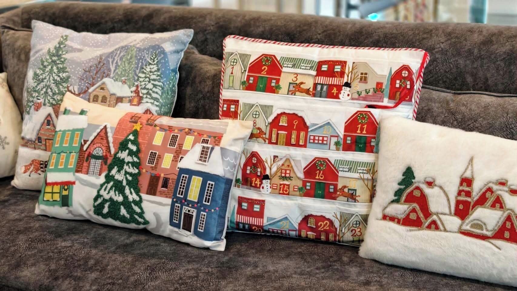 Een bank met meerdere decoratieve kussens met wintertaferelen en landhuizen.