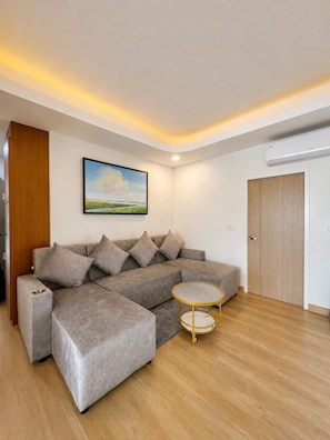A modern living room with a sectional sofa, a round coffee table, and a painting on the wall. - Dview Golden Triangle Hotel Chiangsaen (Chiang Saen)