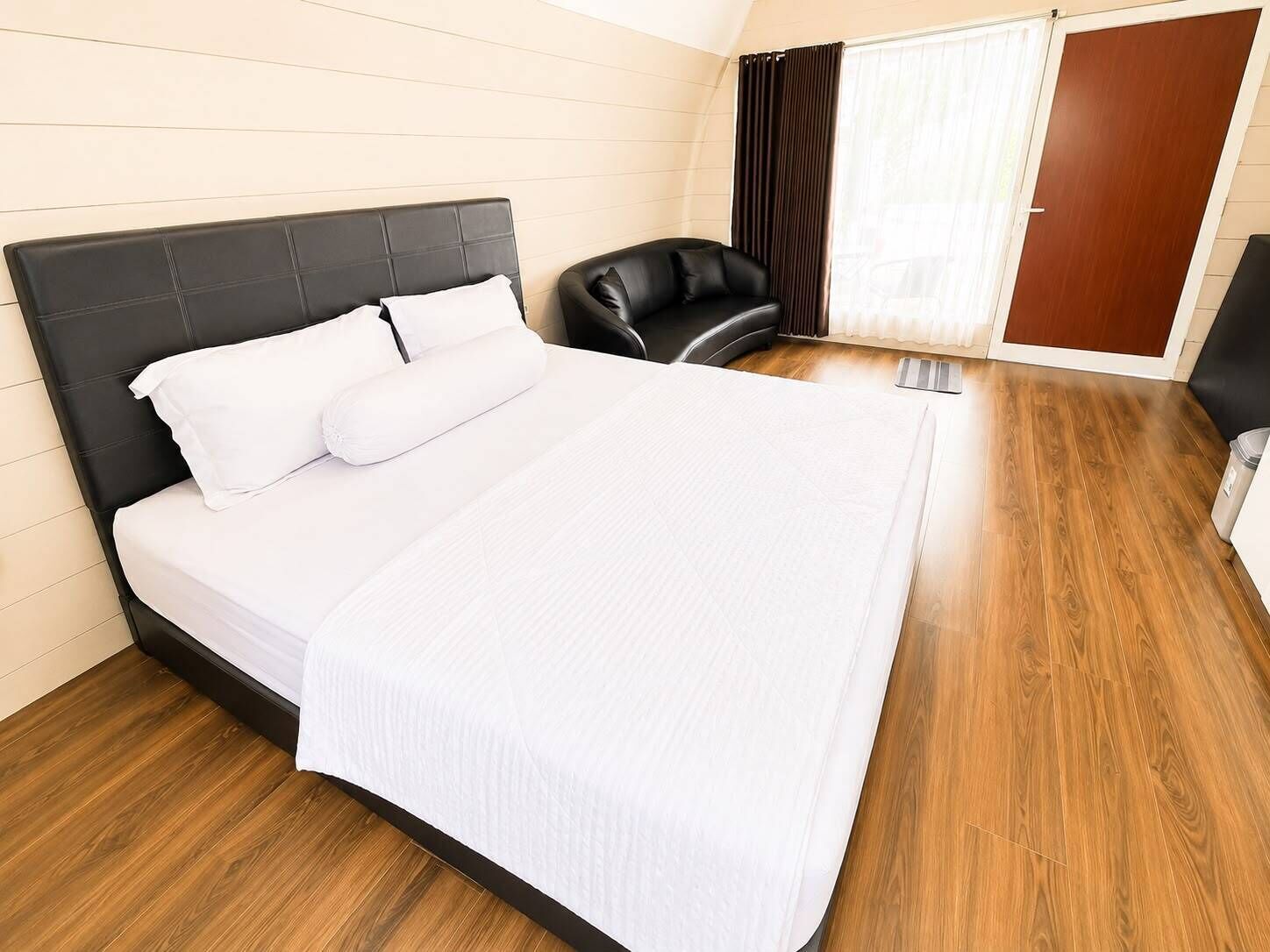 Een moderne hotelkamer met een groot bed, een zwarte leren fauteuil en een houten vloer.