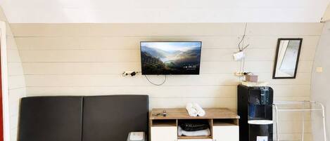 A room with a wooden floor, a black sofa, a TV mounted on the wall, a water dispenser, and a small trash bin.