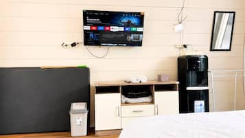 Habitación de hotel con cama, escritorio con monitor de computadora, dispensador de agua y basurero.