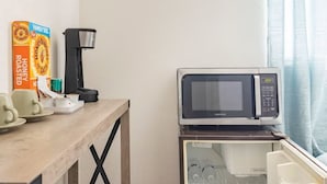 A kitchenette with a microwave, a coffee maker, and breakfast items like honey buns and roasted oats.