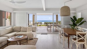 A modern living room with a sofa, coffee table, and dining area. - 3/39 Albatross Avenue (Mermaid Beach)