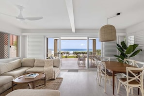 A modern living room with a sofa, coffee table, and dining area. - 3/39 Albatross Avenue (Mermaid Beach)