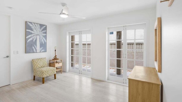 A spacious room with a wooden floor, a ceiling fan, a chair, a small table, and a large window with a view of a wooden deck. - 3/39 Albatross Avenue (Mermaid Beach)