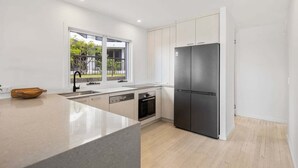 A modern kitchen with a large island, stainless steel appliances, and a view of greenery outside. - 3/39 Albatross Avenue (Mermaid Beach)