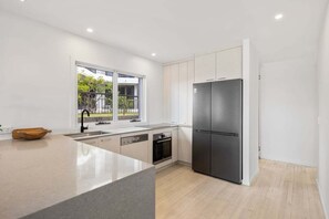 A modern kitchen with a large island, stainless steel appliances, and a view of greenery outside. - 3/39 Albatross Avenue (Mermaid Beach)