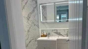 A bathroom with a marble wall, a mirror, a sink, and cabinets.