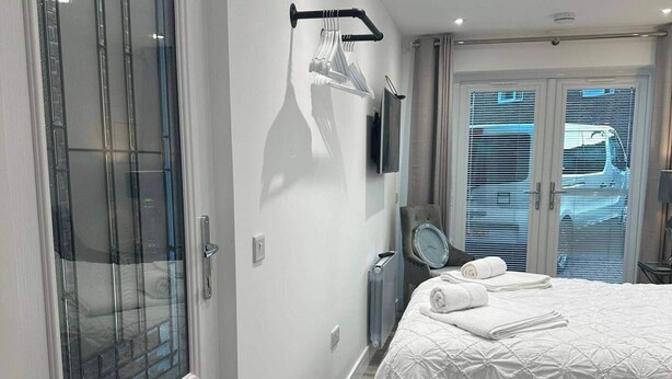 Ett hotellrum med en säng, ett fönster med persienner, ett element och en väggklocka.