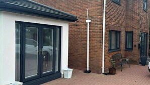 En bostadsbyggnad med en fasad av tegel, en svartsmygad skjutdörr, en vit soptunna och en bänk.