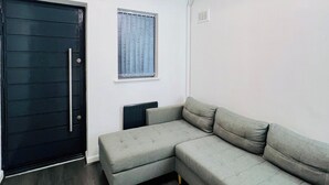 A room with a sectional sofa, a black door, a window with curtains, and a ceiling light fixture. - Hockley 4-Bed, Sleeps 13 w/ Garden & Free Parking (Birmingham)