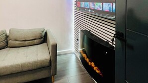 A living room with a sofa, a fireplace, and a mounted TV displaying a streaming service interface. - Hockley 4-Bed, Sleeps 13 w/ Garden & Free Parking (Birmingham)